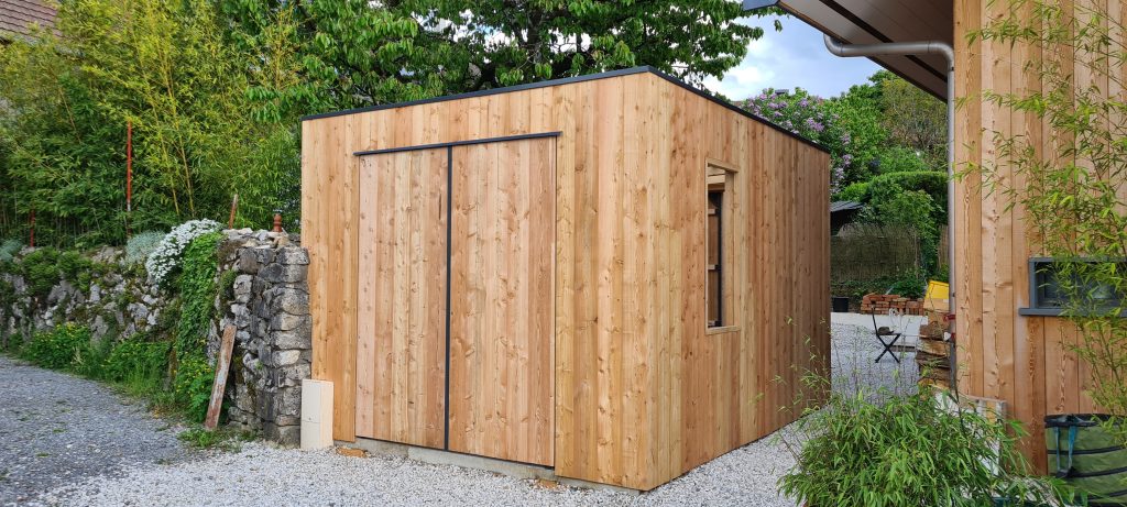 Abri de jardin contemporain en bois, situé à Menthon-Saint-Bernard, conçu par DDLP Structures Bois. Utilisation de bois local avec une finition moderne. Cet abri polyvalent peut servir d'atelier ou de rangement extérieur, tout en s'intégrant parfaitement dans l'environnement naturel.